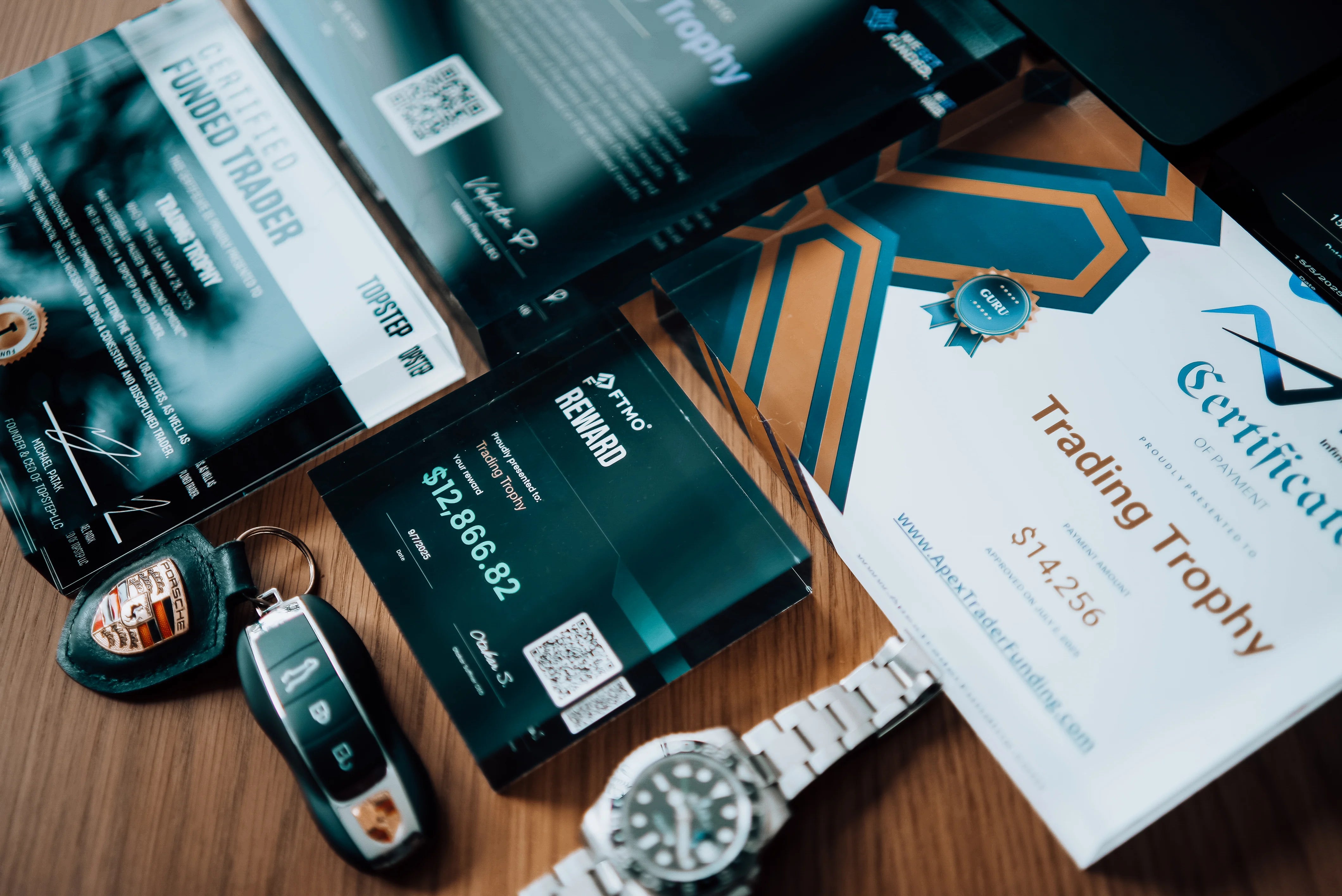 different sizes trading trophy with luxury rolex watch and key's porsche on table